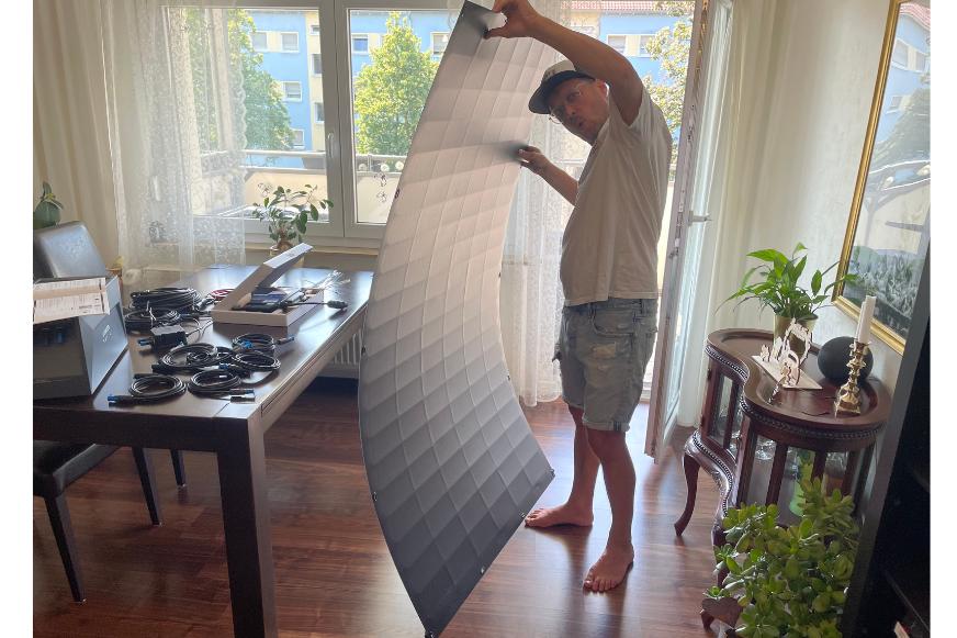 Der Experte hält das leichte und flexible rechteckige Solarmodul neben sich und zeigt die Größe im Vergleich zur Person und man sieht, dass es etwas größer ist als die Test-Person.